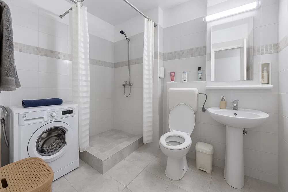 A white bathroom with toilet, laundry and laundry