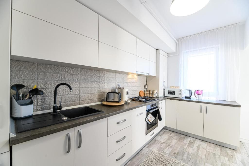 A kitchen with white cabinets and a window — apartment in Brașov
