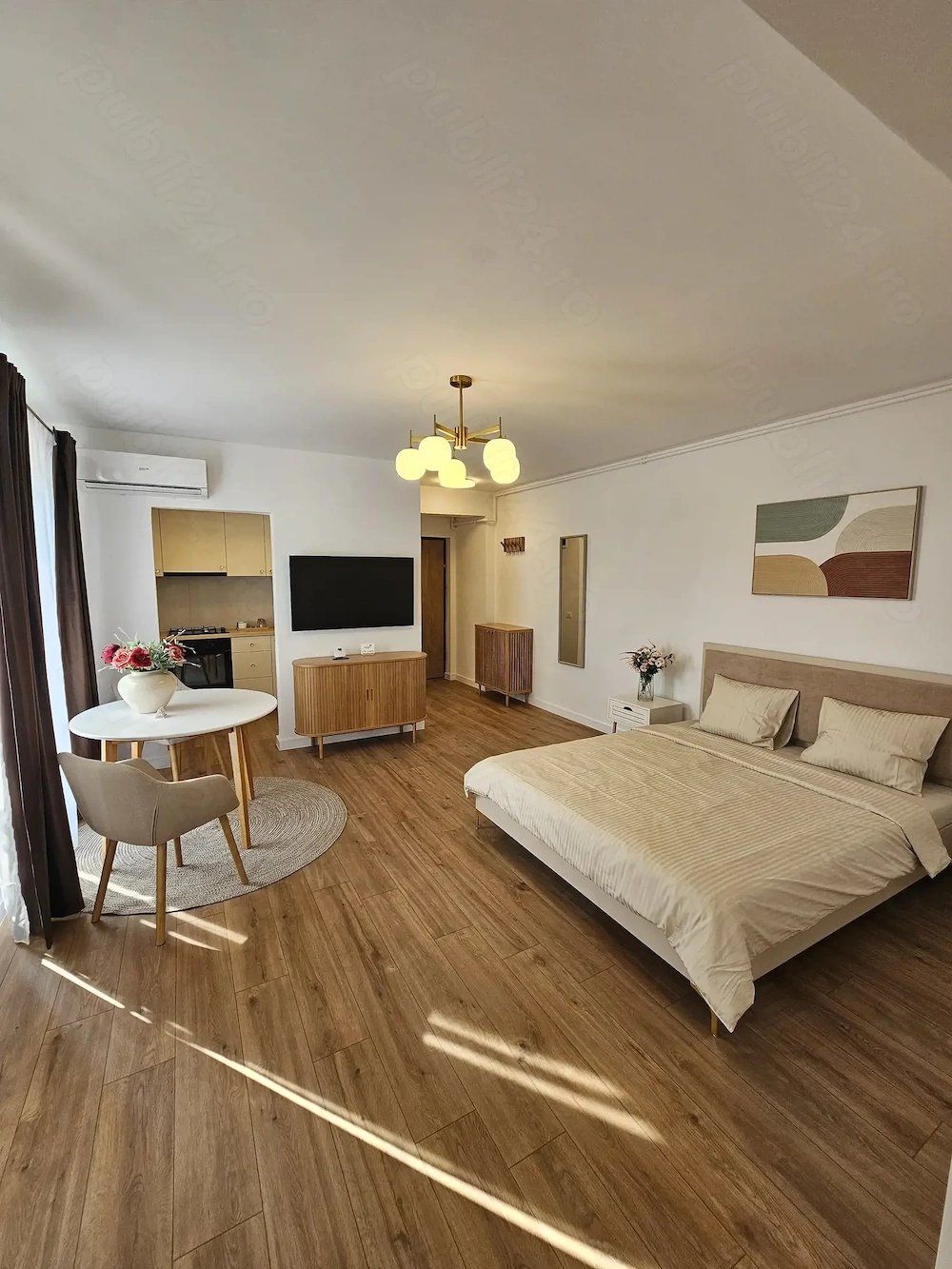 A bedroom with a bed, a table, a chair, a TV, and a window