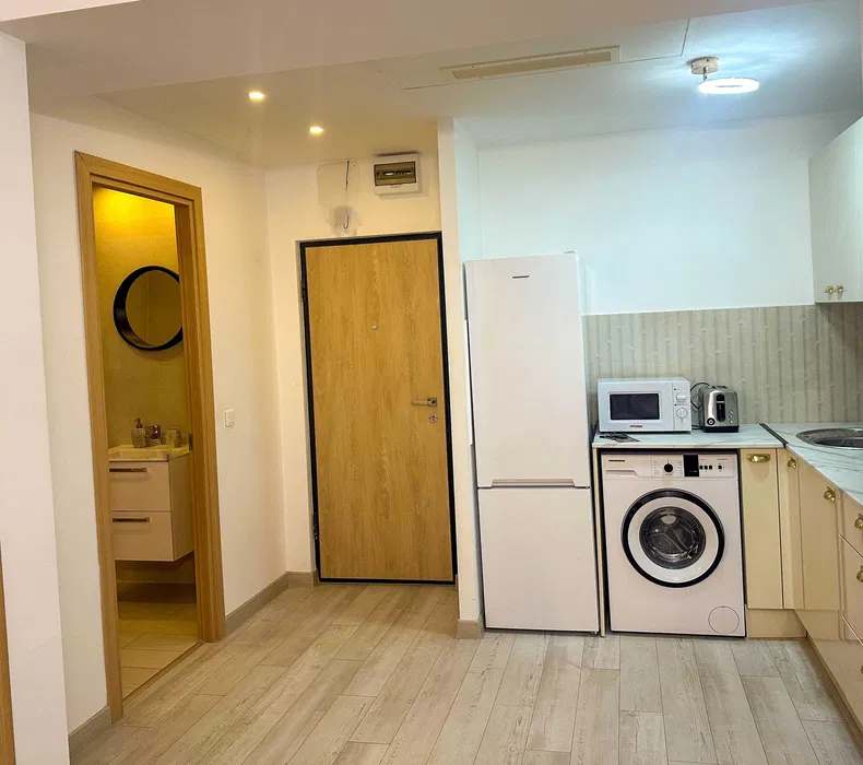 A small, clean, white room with a fridge, washing machine, and microwave — apartment in Bucuresti