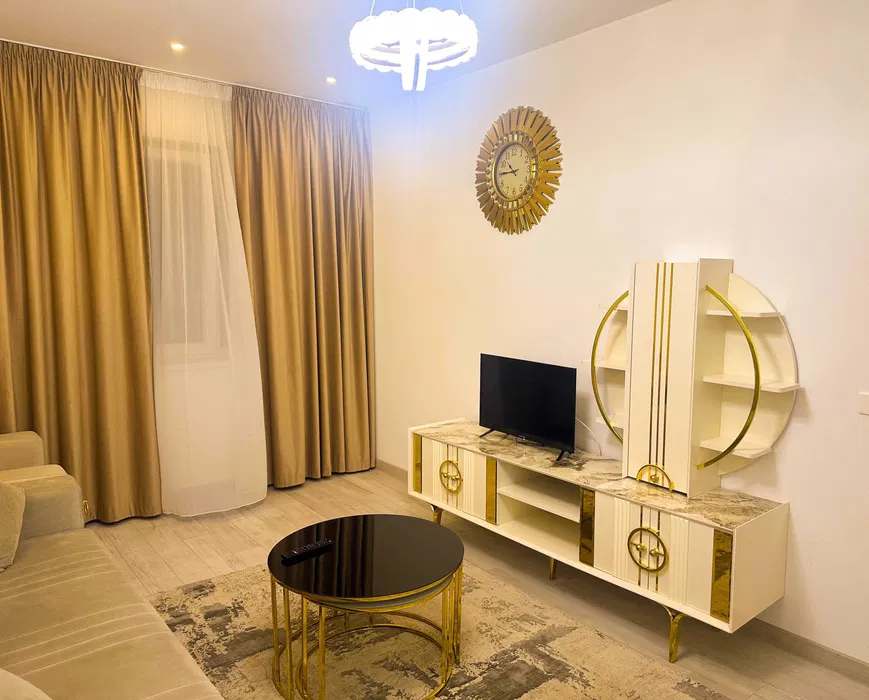 A living room with a flat-screen TV, a table and a clock — apartment in Bucuresti